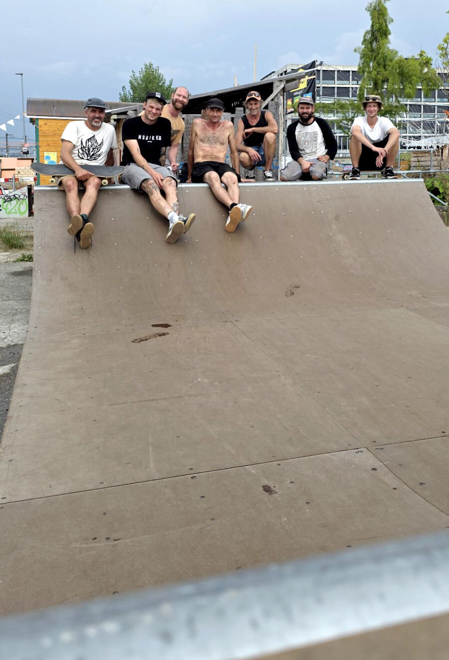 Sieben junge Männer sitzen entspannt auf dem einen Teil der neuen Miniramp und schauen lächelnd und zufrieden in die Kamera. Einer der Männer hält ein Skateboard in den Händen.
