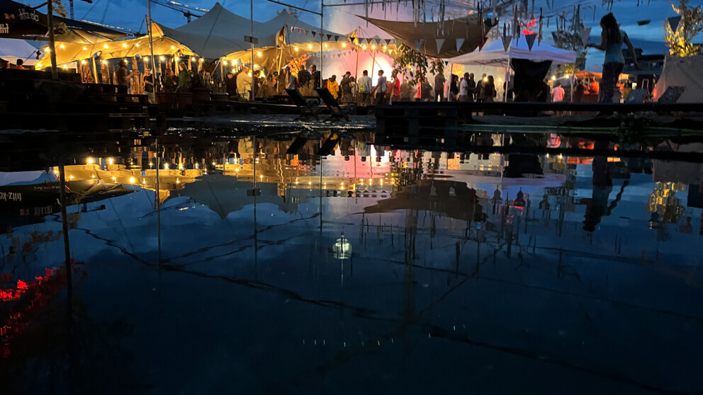 Party-Stimmung auf dem Terrain Sud: Die Lichter reflektieren sich im Wasser, das sich vom vielen Regen auf dem Platz neben dem Sandkasten gesammelt hat.
