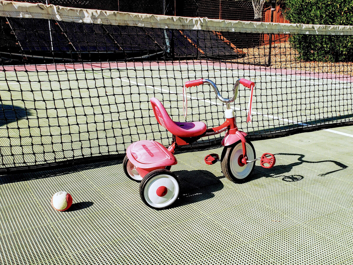 Roter Dreirad vor Tennisnetz auf grünem Tennisplatz